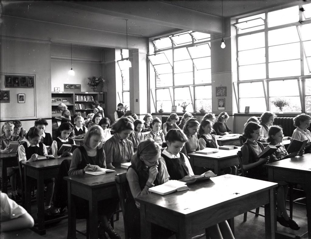 Pupils reading and writing at long tables in a secondary school library, 1945.
